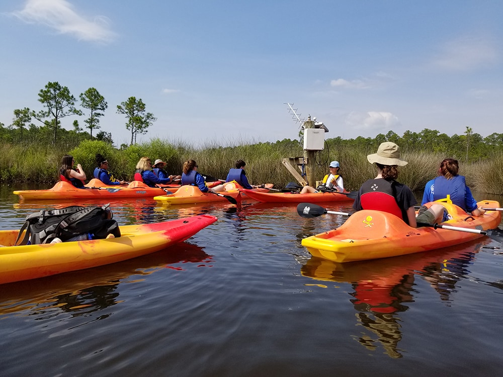 Students in kayaks listening to an instructor speak